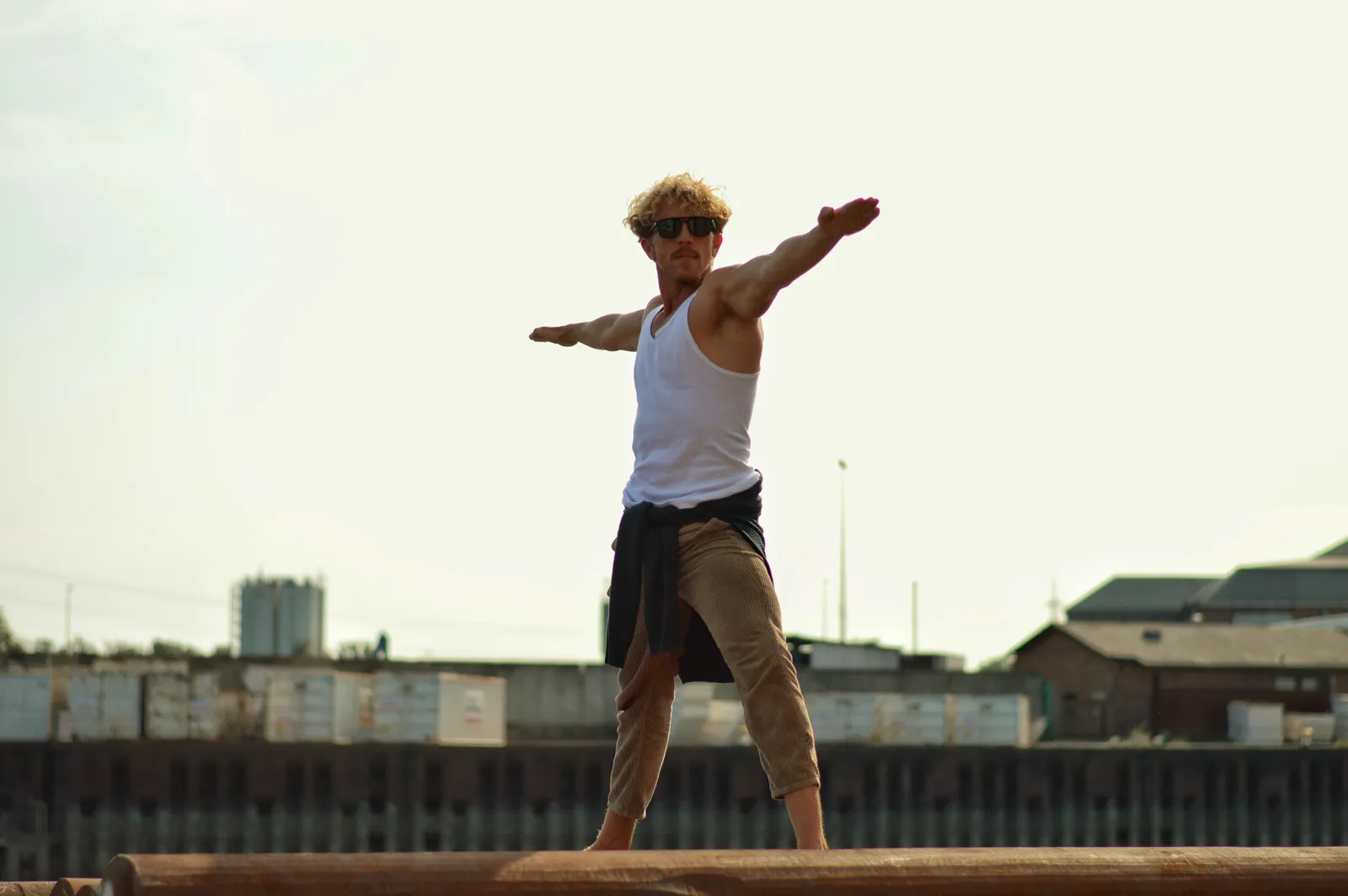 Mann in Warrior-Yoga-Pose auf Holzstämmen, selbstsichere Haltung, urbane Outdoor-Umgebung.