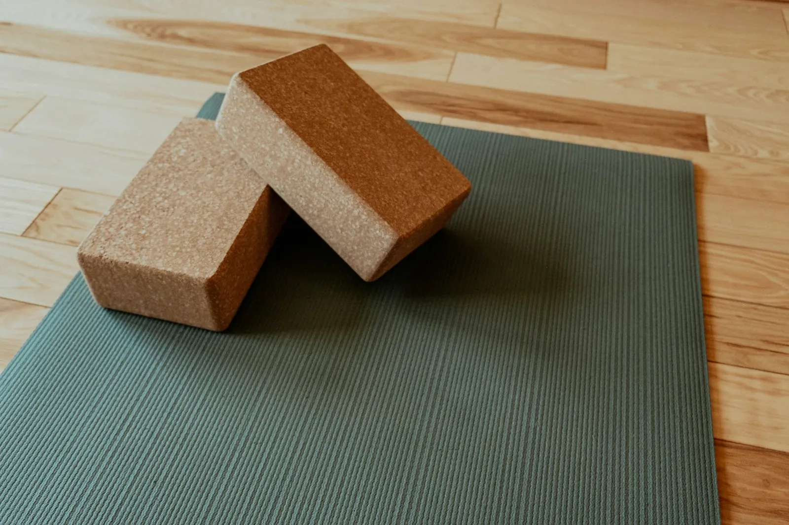 Zwei Korken-Yogablöcke liegen flach auf einer graugrünen, strukturierten Yogamatte auf hellem Holzboden.