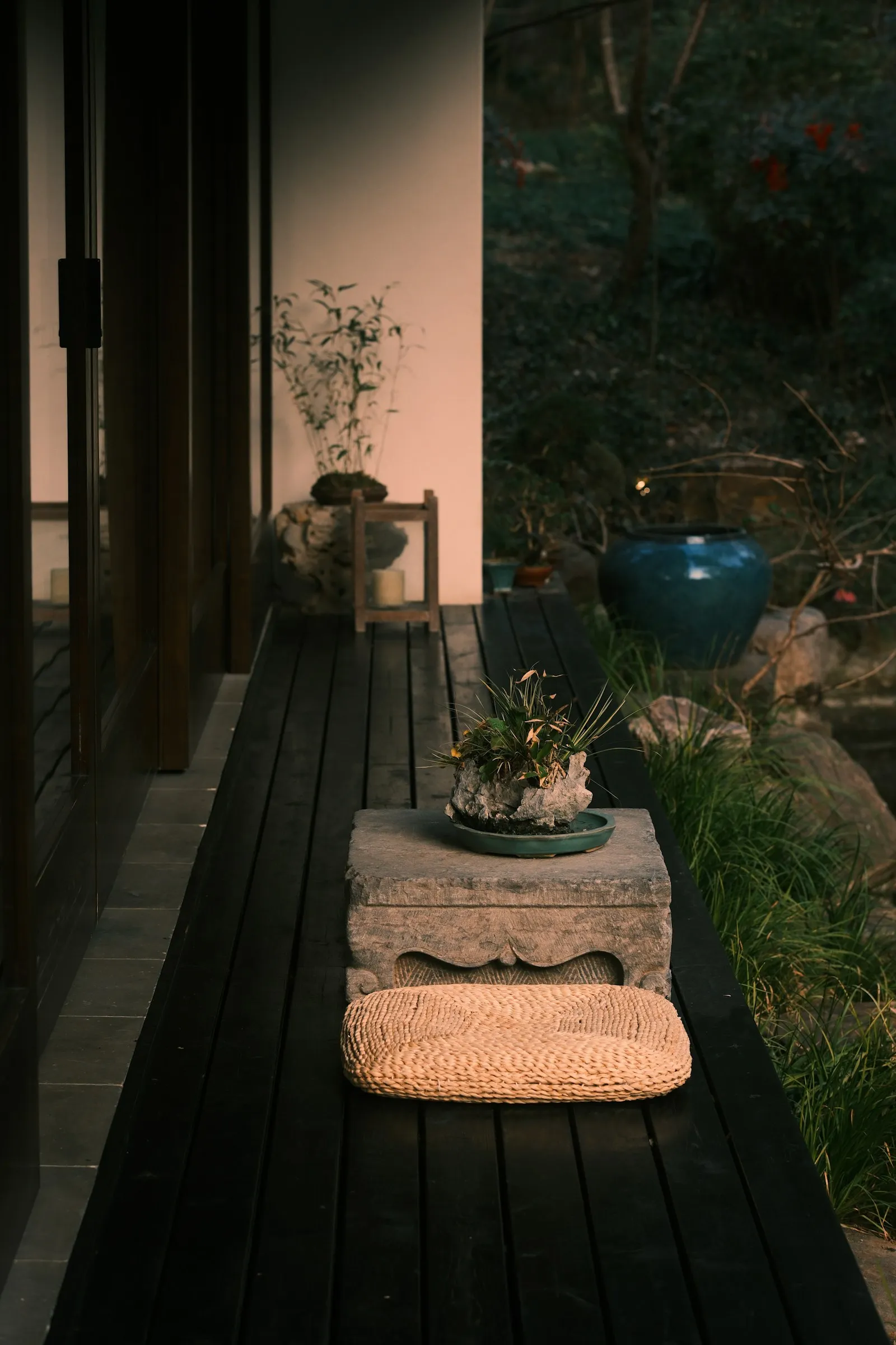 Eine niedrige Holzbank für Meditation steht auf einer Steinterrasse im Abendlicht, daneben eine Sukkulente im Topf und Natursteine.