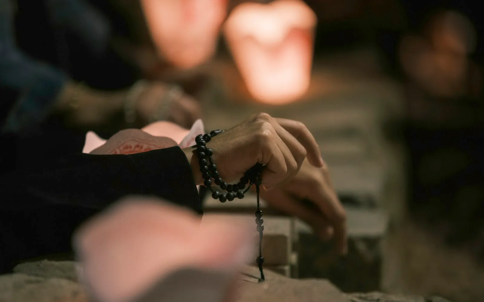 Zwei Hände halten eine Mala-Kette aus dunklen Holzperlen, im Hintergrund weiches Kerzenlicht.