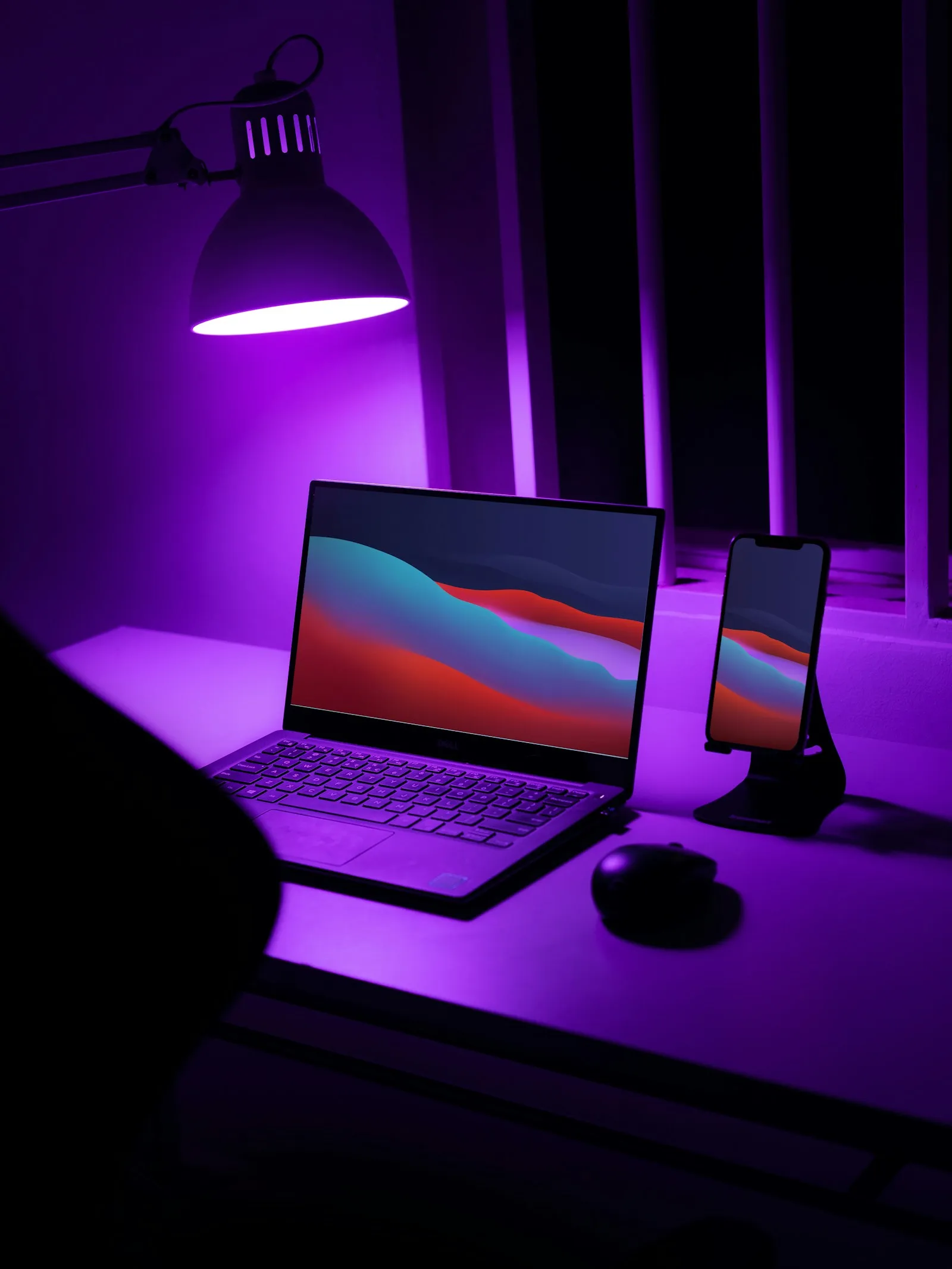 Ein leuchtender Laptop mit violett-orangem Licht steht bei Nacht auf einem Schreibtisch, der Raum um ihn herum liegt im Dunkeln.