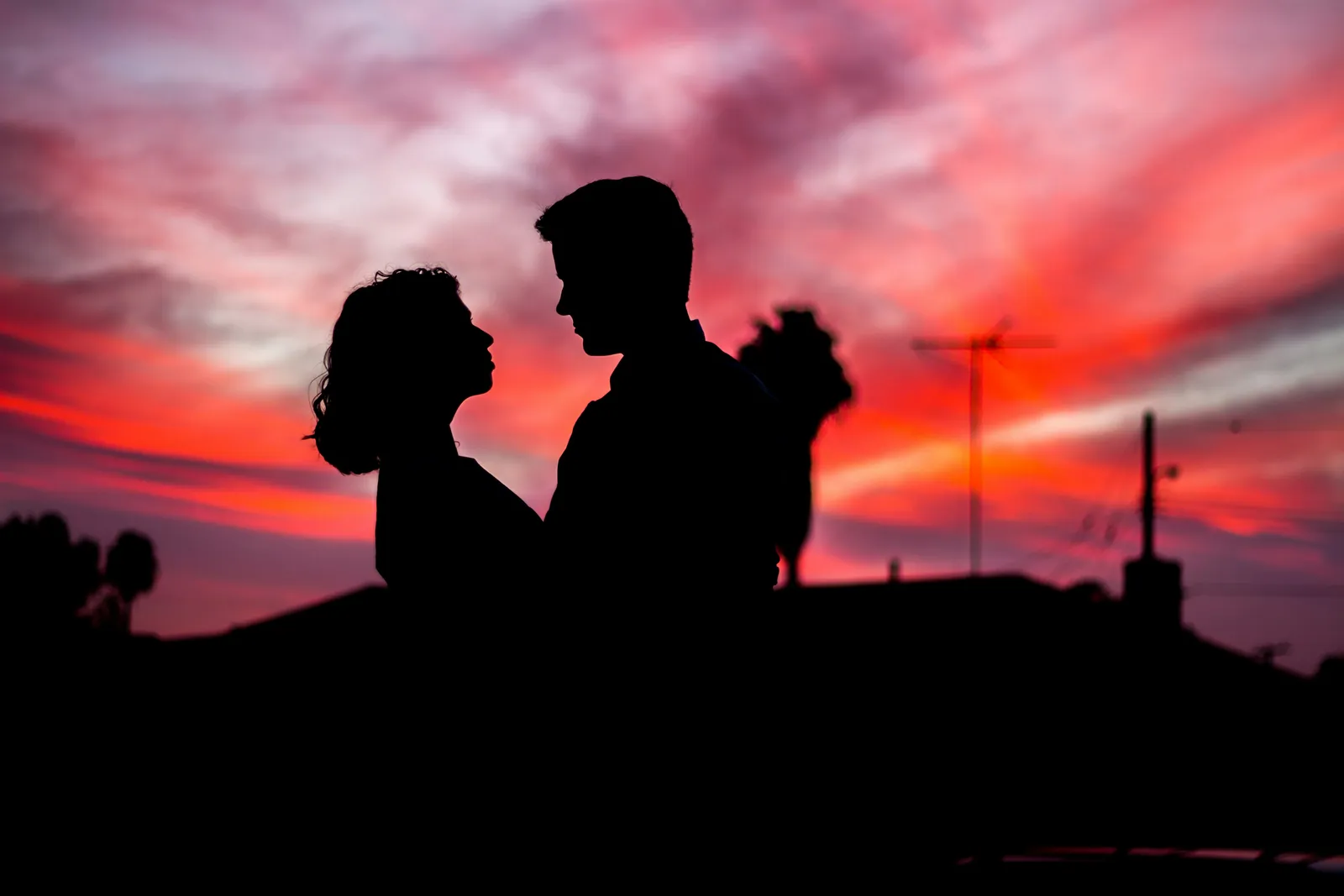 Silhouette eines Paars im Halbprofil gegenüber sitzend vor einem rosa-roten Abendhimmel.