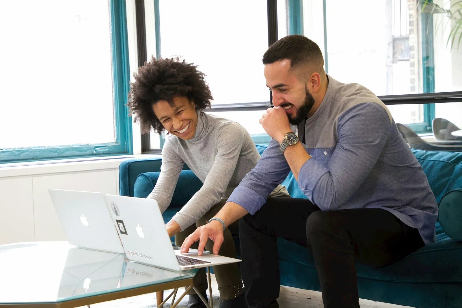 Fünf junge Fachleute sitzen um einen Meetingtisch mit Laptop in einem hellen büro mit Glaswänden und diskutieren lebhaft.