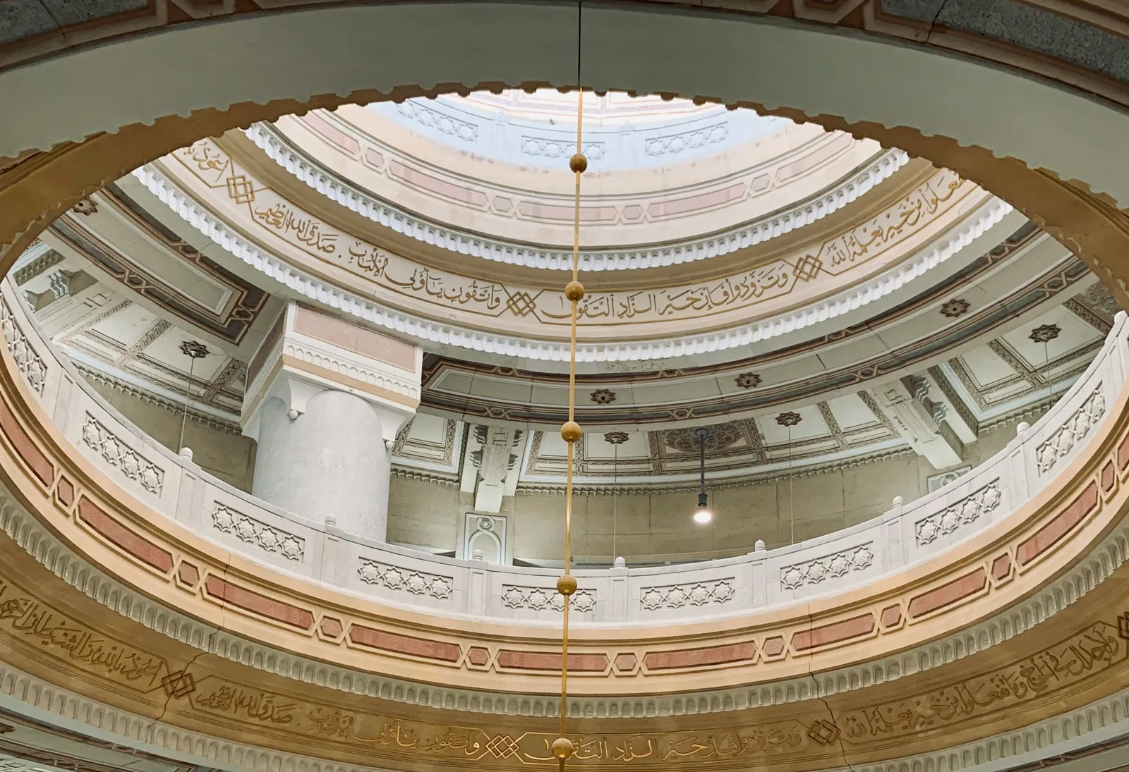 Blick von unten in eine ornate Moschee-Kuppel mit arabischer Kalligraphie und gewölbten Balkonen.