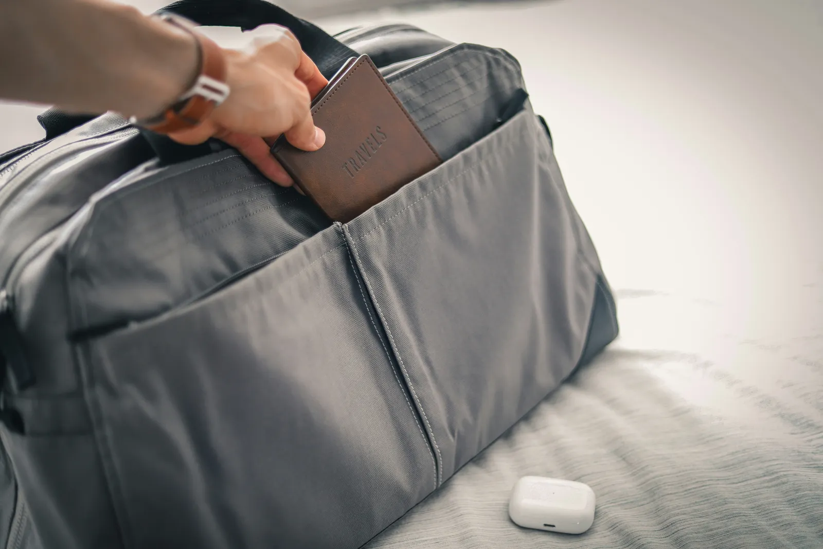 Hand zieht ein Reisetagebuch aus einem grauen Reisetaschen-Seitenfach, Vorbereitung auf ein Selbstentdeckungs-Retreat.