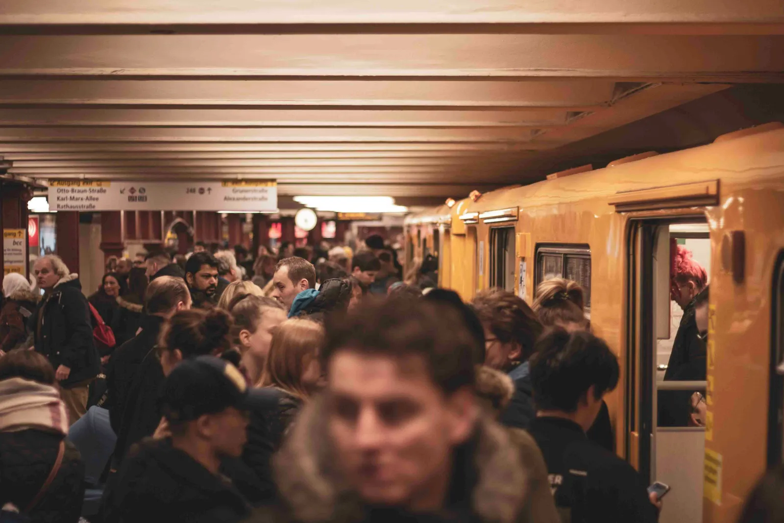 Überfüllter U-Bahnsteig mit aussteigenden Pendlern aus einem gelben Zug, deutsche Beschilderung über dem Bahnsteig.