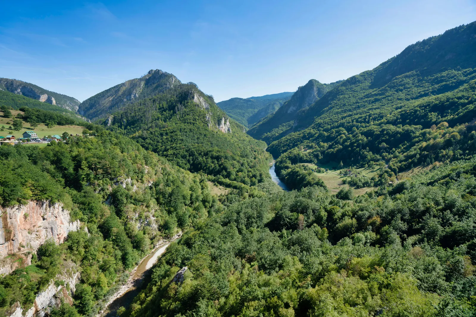 Weites, grünes Flusstal mit steilen bewaldeten Hängen unter blauem Himmel, menschenleere Naturlandschaft.