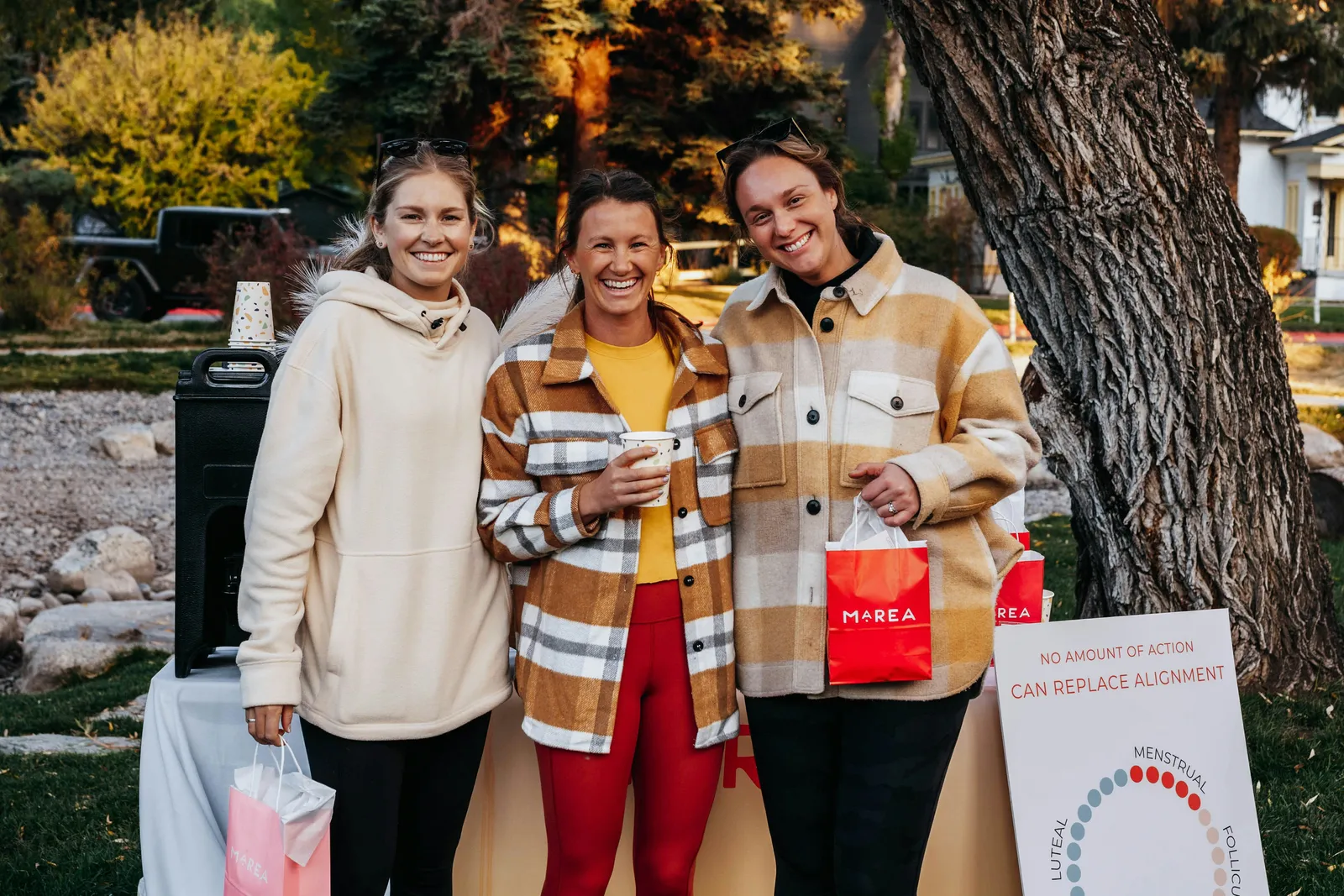 Drei Frauen lachen gemeinsam im Freien in herbstlicher Kleidung bei einem Wellness-Treffen, warme Herbststimmung.
