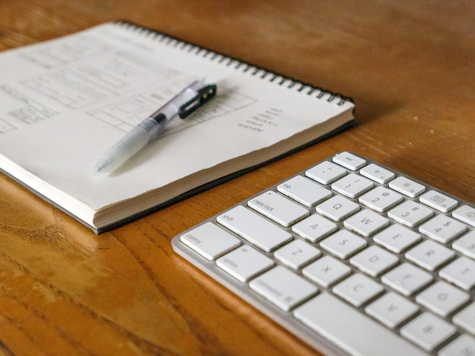 Ein offenes Spiralheft mit einem Stift neben einer Tastatur auf einem Holzschreibtisch, die Werkzeuge einer Journaling-Praxis.