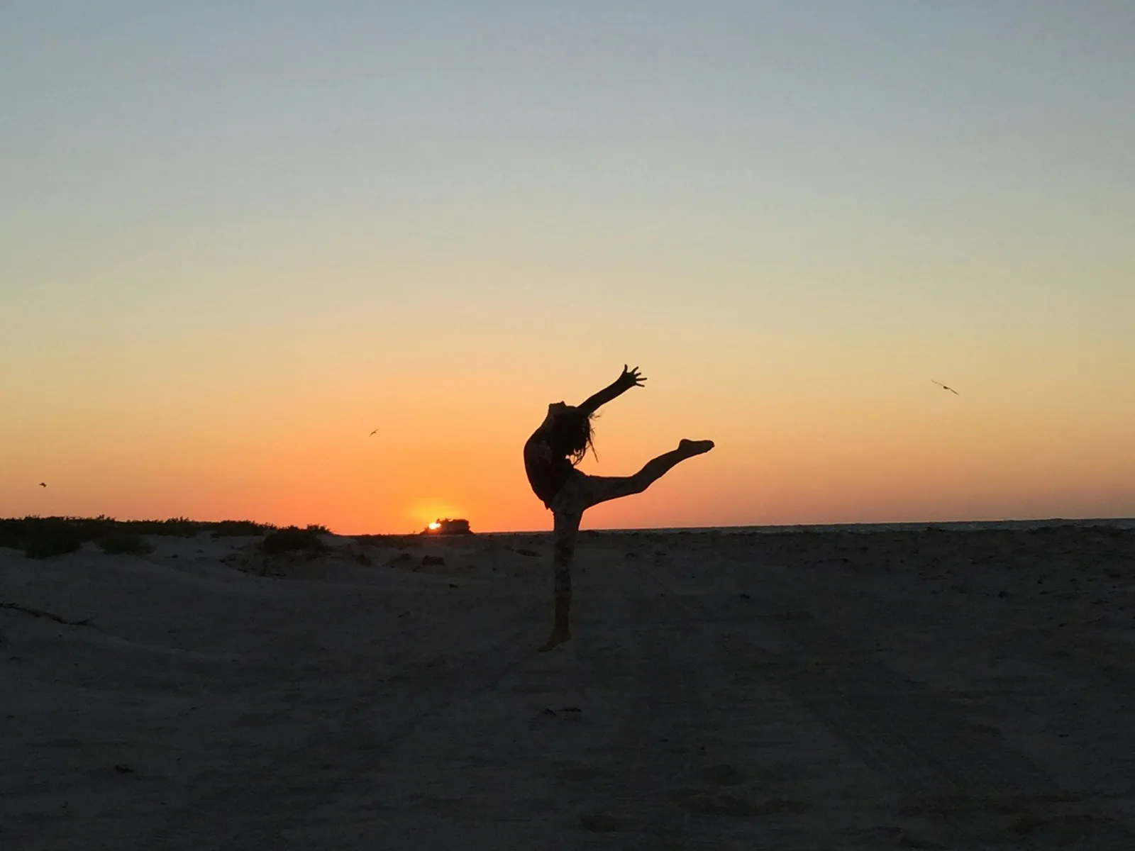 Silhouette einer Frau in einer Steh-Yoga-Pose am Sandstrand bei Sonnenuntergang