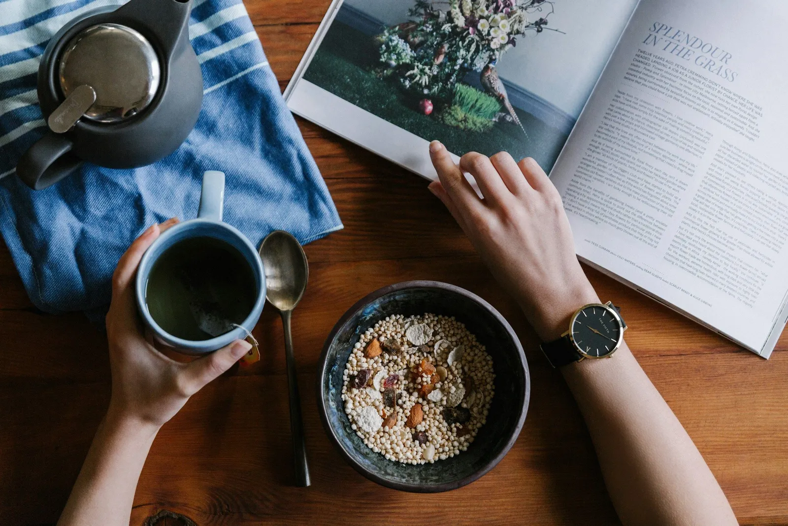 Vogelperspektive auf Hände die eine Kaffeetasse halten, neben einer Müsli-Schüssel auf Holztisch: das ruhige Morgenritual eines Yoga-Retreats.